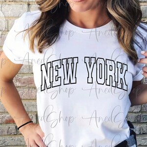 May include: White t-shirt with black text that reads "NEW YORK" in a collegiate font.