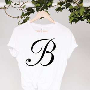 May include: White t-shirt with a black cursive letter "B" on the front.