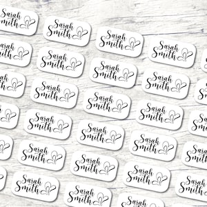 May include: Twenty-four white rectangular labels with the text "Sarah Smith" and a heart design printed in black.