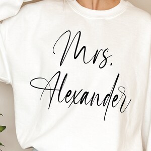 May include: White sweatshirt with the text "Mrs. Alexander" in black cursive script.