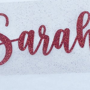 May include: Red glitter vinyl decal with the name "Sarah" written in a cursive font.