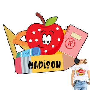 May include: A red apple with white polka dots and a smiling face, surrounded by school supplies including a pencil, eraser, ruler, and a notebook with an A+ grade. The pencil has the name "MADISON" written on it.