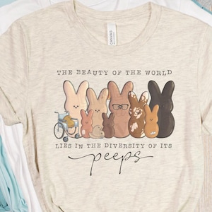 May include: A beige t-shirt with a graphic of a group of colorful Peeps marshmallow candies. The text "The beauty of the world lies in the diversity of its peeps" is printed on the shirt.