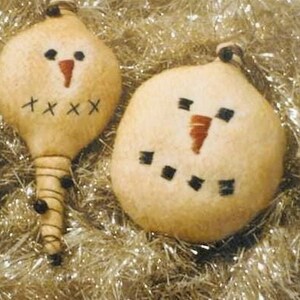 May include: Three handmade snowman ornaments with stitched details. The snowmen have carrot noses, black eyes, and stitched mouths. One is elongated, and the others are round. The ornaments are beige and sit on a bed of silver tinsel.