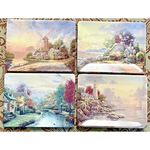 May include: Set of four rectangular decorative plates featuring scenic landscape paintings. Each plate depicts a different picturesque scene: a windmill, a cottage, a river scene, and a lighthouse. The plates have a glossy finish and are likely made of ceramic.