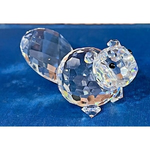 May include: A clear crystal squirrel figurine with a faceted design. The squirrel has a large, bushy tail and small, black eyes. The figurine is displayed on a blue surface.