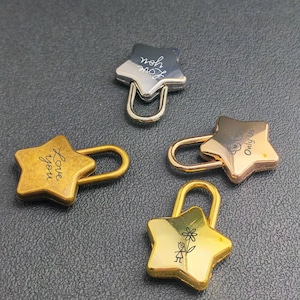 Puede incluir: Cuatro candados en forma de estrella en tonos plateado, dorado y bronce. Un candado plateado tiene grabado "Love you". Otro candado dorado tiene una flor y un hombrecito. Los otros dos tienen grabados "Love you" y "Only us".