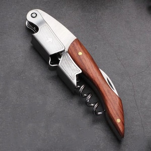 May include: A silver and wood wine opener with a corkscrew and a foil cutter. The handle is made of dark wood with gold accents.