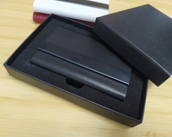 May include: A black leather business card holder with a black metal trim is displayed in a black box with a black velvet lining.