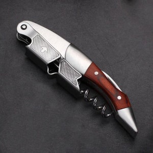 May include: A silver and wood wine bottle opener with a corkscrew and a lever. The opener has a wood handle with a red stain.