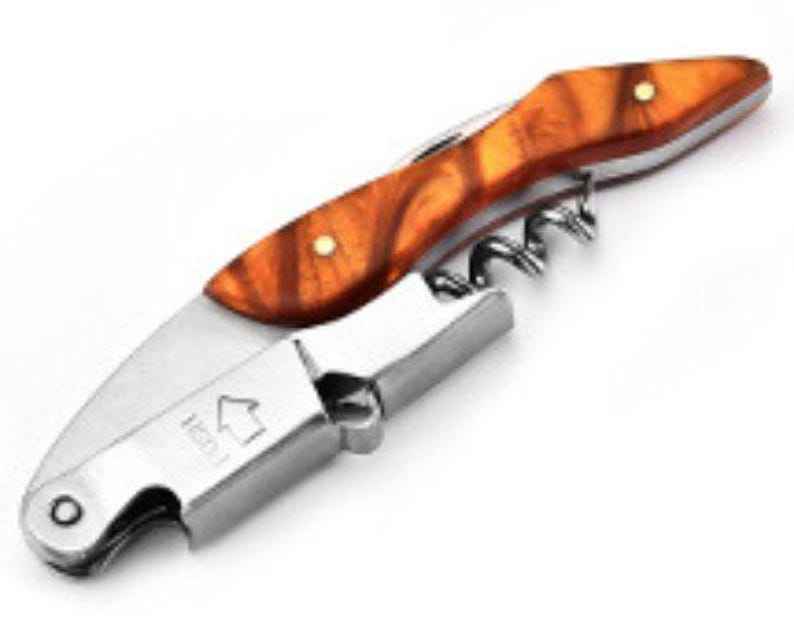 May include: A stainless steel waiter's corkscrew featuring a handle with a polished amber-colored wood grain pattern and two brass rivets. The metal body includes a folding spiral worm, a lever arm, and the word PUSH with an upward-pointing arrow.
