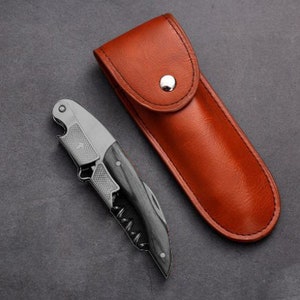 May include: A silver and black corkscrew with a wooden handle, in a brown leather carrying case.