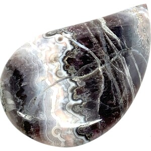 May include: A teardrop-shaped cabochon of purple and white agate with a swirling pattern. The stone is polished and has a smooth surface.