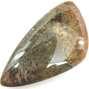 May include: A clear, faceted, teardrop-shaped gemstone with brown and gold inclusions. The gemstone has a smooth, polished surface.