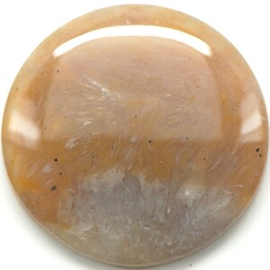 May include: A polished, round gemstone with a warm color palette. The stone features a blend of peach, tan, and cream hues, with subtle white and gray veining patterns. Small dark specks are scattered across the surface, adding depth.