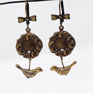 May include: A pair of gold-toned earrings featuring a bird charm and a decorative filigree design. The earrings have a bow-shaped hook.