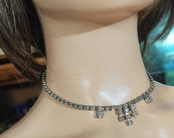 May include: Silver-toned rhinestone choker necklace. The necklace features a delicate chain adorned with small, sparkling rhinestones. A cluster of larger rhinestones hangs from the center, adding a touch of elegance to this jewelry piece.