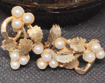 May include: A pair of vintage clip-on earrings. Each earring features a gold-toned, leaf-like design with clusters of small, round, faux pearls. The earrings have a classic, elegant style, suitable for formal occasions.