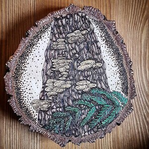 May include: A wood slice with a detailed black and white drawing of a tree trunk with mushrooms growing on it. The tree trunk is surrounded by green fern-like plants.
