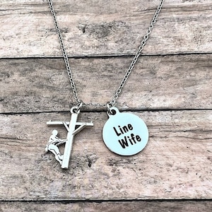 May include: Silver necklace with a charm of a lineman climbing a utility pole and a round charm that says "Line Wife".