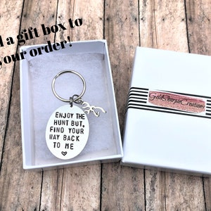 May include: A silver key chain with a round charm that says "Enjoy the hunt but, find your way back to me" with a small heart symbol. The key chain is in a white gift box with a black and white striped ribbon.