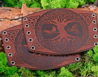 May include: Two brown leather bracelets with a Celtic knot design and a tree of life motif. The bracelets have silver eyelets and are embossed with a dark brown color.