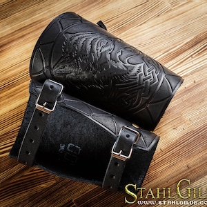 May include: A pair of black leather arm guards featuring a wolf design and Celtic knotwork. The guards have adjustable straps with silver buckles.