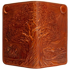 May include: Brown leather wallet with an embossed tree design. The wallet features a detailed landscape with a tree, mountains, sun, and moon. The name "STAN GILDE" is embossed at the bottom. The wallet is rectangular and has a stitched border.