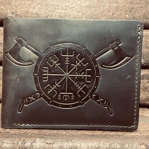 May include: Dark gray leather wallet featuring a detailed embossed design. The design includes a central circular emblem with intricate symbols, flanked by two crossed axes. The wallet is rectangular and appears to be new.