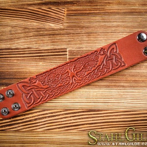 May include: A brown leather bracelet with a Celtic knot design and a tree of life motif. The bracelet has silver-toned metal rivets.