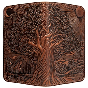 May include: Brown leather wallet with a detailed embossed design of a large tree, mountains, sun, and moon. The wallet has the text "STAHL GILDE" at the bottom. The design is intricate and the color is a rich brown.