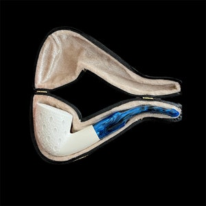 Könnte beinhalten: Eine weiße Pfeife mit einem blauen und schwarzen marmorierten Schaft in einem schwarzen, samtenen Etui.