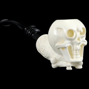 May include: A white skull-shaped pipe with a black stem. The skull has detailed features, including eye sockets, a nose, and a mouth with teeth.