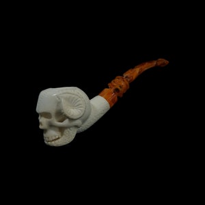 May include: A white skull pipe with a brown stem. The skull has horns and a detailed carving.