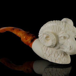 May include: A white meerschaum pipe carved in the shape of a ram's head with curled horns. The pipe has a brown amber stem.