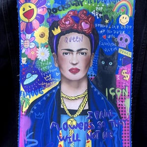 Può includere: Una giacca di jeans blu con una toppa colorata che presenta un ritratto di Frida Kahlo con il testo "Rockstar Revolution", "Queen", "Frida Freepa Freedom", "Famous", "I paint flowers so they will not die", "Icon" e "Power".