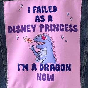 Puede incluir: Chaqueta vaquera con un parche rosa con el texto "I Failed As A Disney Princess I'm A Dragon Now". El parche incluye un dragón de dibujos animados con gafas de sol en forma de corazón.