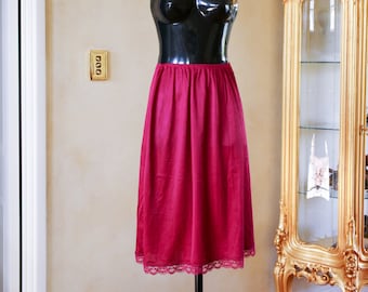May include: A knee-length magenta skirt featuring a smooth, solid-colored fabric with a delicate lace trim along the bottom hem. The skirt has a simple, straight silhouette and is displayed on a black mannequin torso with a silver necklace.