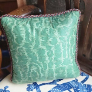 Puede incluir: Una almohada verde y blanca con estampado y ribete rojo y azul. La almohada est&aacute; sentada en una silla con estampado floral blanco y azul.