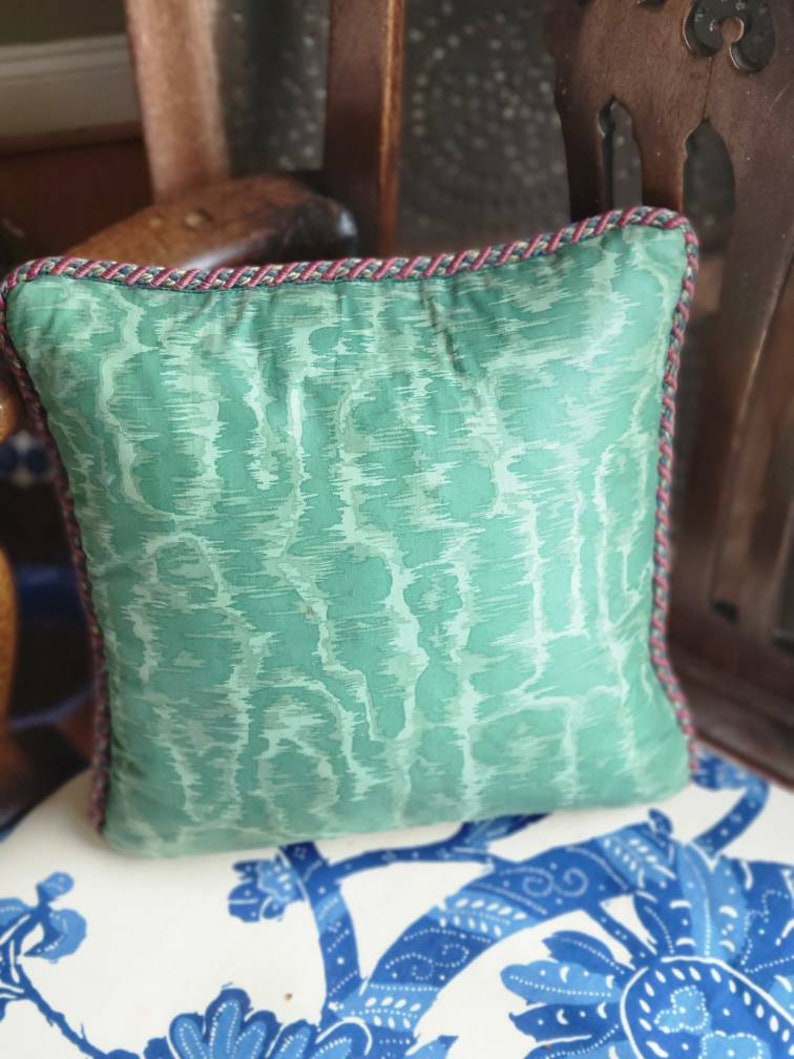 Puede incluir: Una almohada verde y blanca con estampado y ribete rojo y azul. La almohada est&aacute; sentada en una silla con estampado floral blanco y azul.