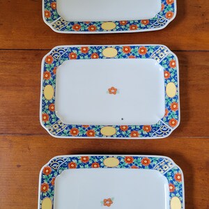May include: Three rectangular ceramic serving platters with blue, green, yellow, and orange floral designs. The platters have white centers and are perfect for serving appetizers, desserts, or snacks.