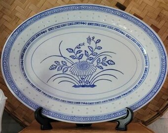 May include: A white oval serving platter with a blue and white floral design. The platter has a blue rim with a repeating diamond pattern.
