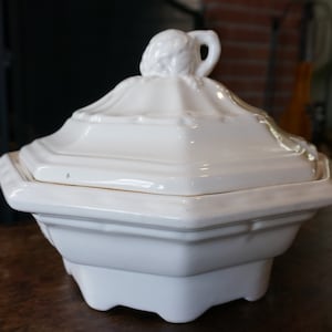 May include: White ceramic serving dish with a lid. The lid has a decorative knob in the shape of a flower.