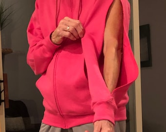 May include: A bright pink zip-up hoodie with open sleeves. The hoodie has a drawstring hood, front pockets, and ribbed cuffs. The zipper is silver. The person is wearing gray sweatpants.