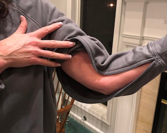 May include: A gray hooded sweatshirt with zippered sleeves. The sleeves are unzipped and rolled up to the elbows. The sweatshirt has a kangaroo pocket. The text on the sign reads "I'm outdoorsy I like getting drunk on patios."