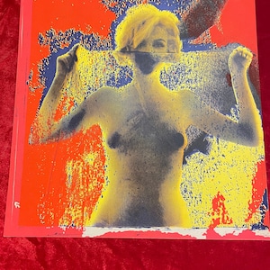 May include: A vintage poster with a woman in a yellow and blue color scheme. The woman is nude and has her arms raised above her head. The background is a red and yellow color scheme.