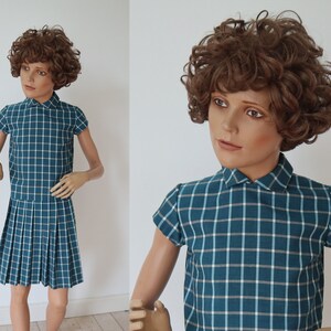May include: A teal plaid dress with short sleeves and a pleated skirt. The dress has a white and light blue grid pattern. The dress is displayed on a mannequin with a brown curly wig.