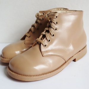 May include: A pair of tan-colored, lace-up ankle boots. The boots have a glossy finish and a rounded toe. The laces and soles are a lighter shade of tan. The boots are likely for children.
