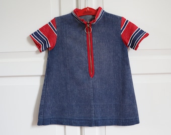 Könnte beinhalten: Blaues Jeanskleid mit rot-weiß gestreiften Ärmeln und einem roten Reißverschluss. Das Kleid hat einen hohen Kragen und einen Reißverschluss mit Ring. Das Kleid hängt an einem roten Kleiderbügel.