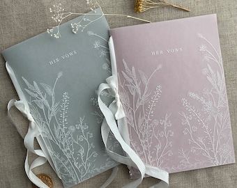 May include: Two white vellum vow books with a floral design and the text "His Vows" and "Her Vows" on the covers. The books are tied together with a white ribbon.